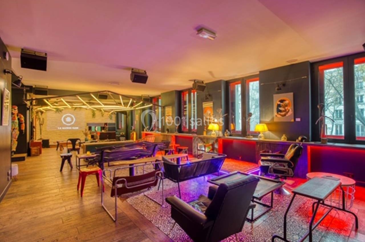 Salle moderne avec mobilier éclectique, éclairage coloré et grandes fenêtres donnant sur un extérieur arboré.