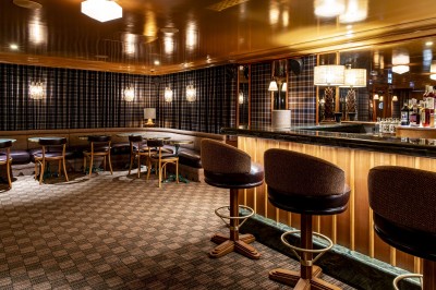 Salle avec tables et chaises en bois, banquettes rouges, murs à motif écossais et éclairage tamisé.