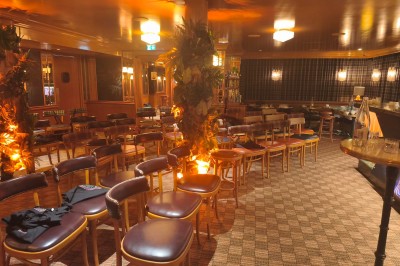 Salle avec tables et chaises en bois, banquettes rouges, murs à motif écossais et éclairage tamisé.