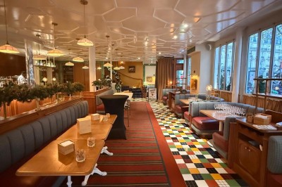 Salle avec tables et chaises en bois, banquettes rouges, murs à motif écossais et éclairage tamisé.