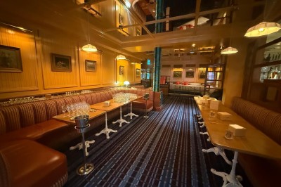 Salle avec tables et chaises en bois, banquettes rouges, murs à motif écossais et éclairage tamisé.