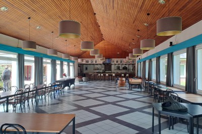 Pelouse verte entourée de bâtiments en briques et crépi, avec arbres et allée en béton sous un ciel dégagé.