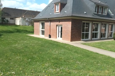 Pelouse verte entourée de bâtiments en briques et crépi, avec arbres et allée en béton sous un ciel dégagé.