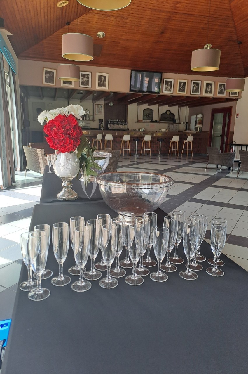 Table dressée avec des flûtes à champagne, un vase de roses rouges et blanches, et un grand saladier dans une salle…