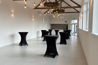 Salle lumineuse avec des rangées de chaises blanches alignées, plafond avec poutres apparentes et décor floral suspendu.