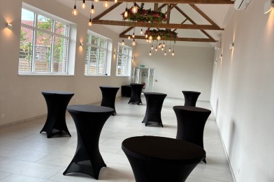 Salle lumineuse avec des rangées de chaises blanches alignées, plafond avec poutres apparentes et décor floral suspendu.