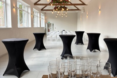 Salle lumineuse avec des rangées de chaises blanches alignées, plafond avec poutres apparentes et décor floral suspendu.