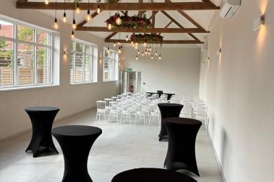 Salle lumineuse avec des rangées de chaises blanches alignées, plafond avec poutres apparentes et décor floral suspendu.