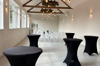 Salle lumineuse avec des rangées de chaises blanches alignées, plafond avec poutres apparentes et décor floral suspendu.
