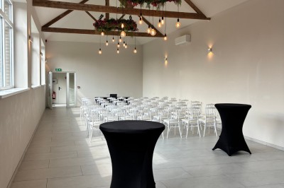 Salle lumineuse avec des rangées de chaises blanches alignées, plafond avec poutres apparentes et décor floral suspendu.