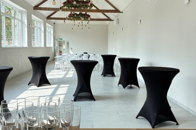 Salle lumineuse avec des rangées de chaises blanches alignées, plafond avec poutres apparentes et décor floral suspendu.