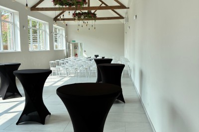 Salle lumineuse avec des rangées de chaises blanches alignées, plafond avec poutres apparentes et décor floral suspendu.
