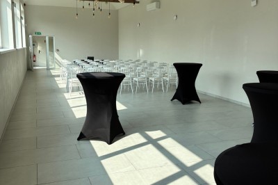 Salle lumineuse avec des rangées de chaises blanches alignées, plafond avec poutres apparentes et décor floral suspendu.