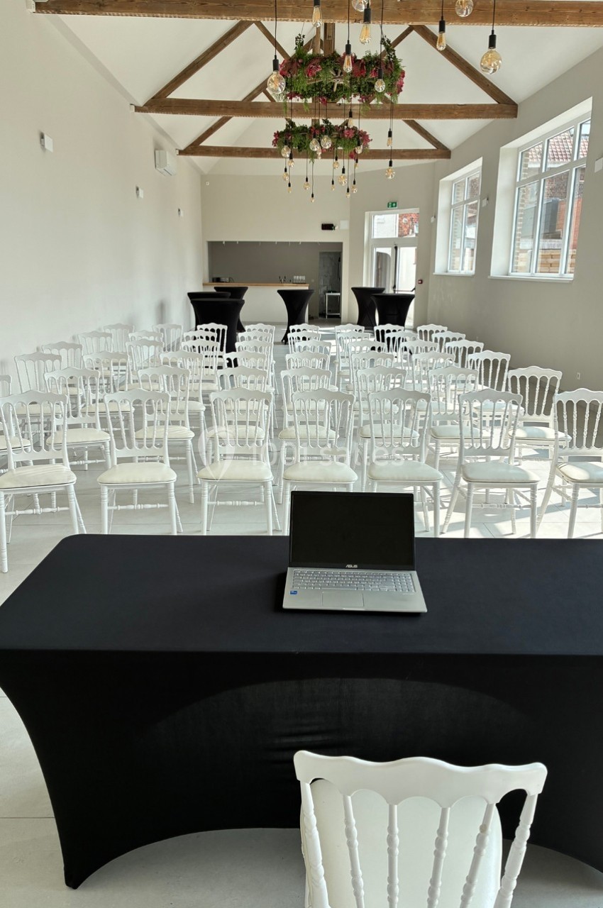 Salle lumineuse aménagée pour une conférence, avec des rangées de chaises blanches et une table noire équipée d'un…