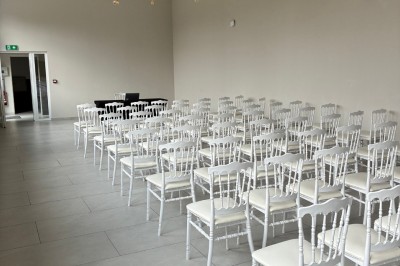 Salle lumineuse avec des rangées de chaises blanches alignées, plafond avec poutres apparentes et décor floral suspendu.