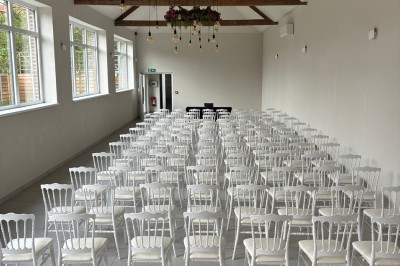 Salle lumineuse avec des rangées de chaises blanches alignées, plafond avec poutres apparentes et décor floral suspendu.