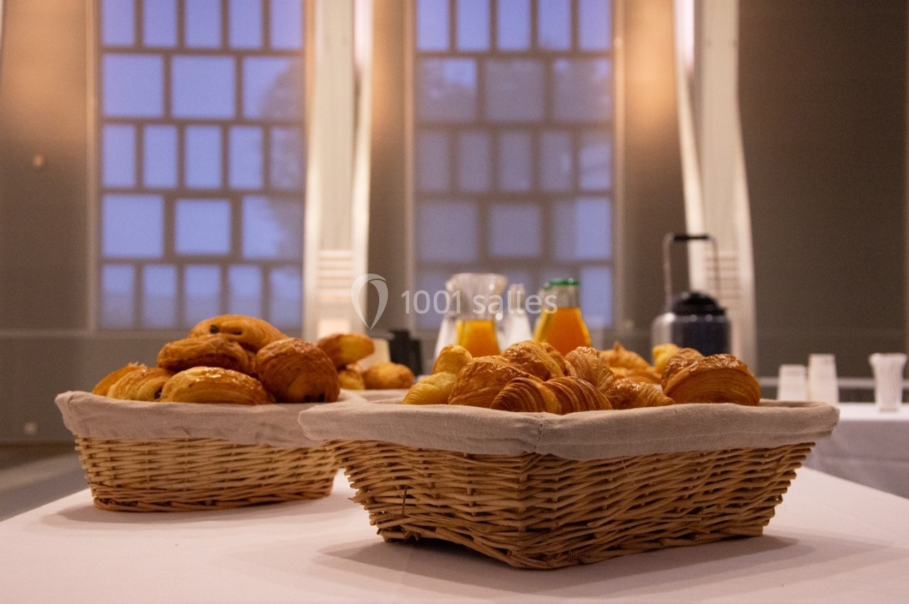 Location salle Mont-de-Marsan (Landes) - Cci des Landes #10 Paniers de viennoiseries avec jus d'orange et cafetière en arrière-plan dans une salle lumineuse.