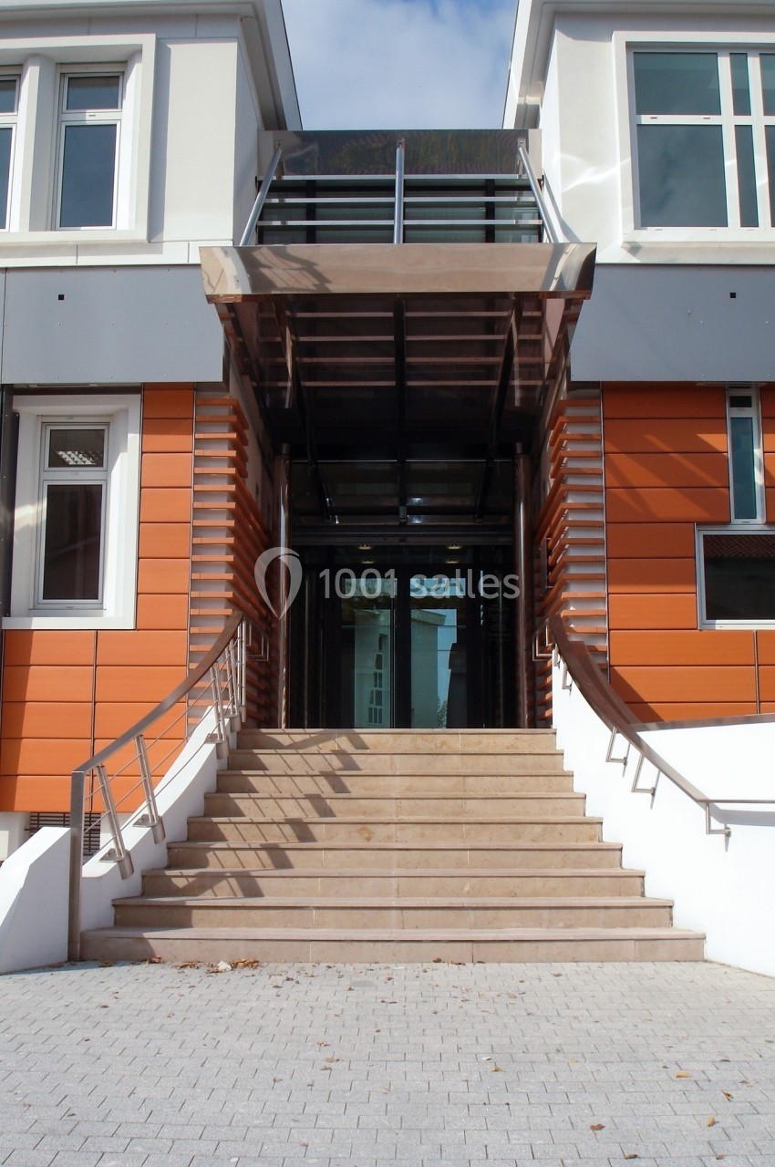 Location salle Mont-de-Marsan (Landes) - Cci des Landes #13 Entrée d'un bâtiment moderne avec escalier central, rampe d'accès et façade orange et blanche.