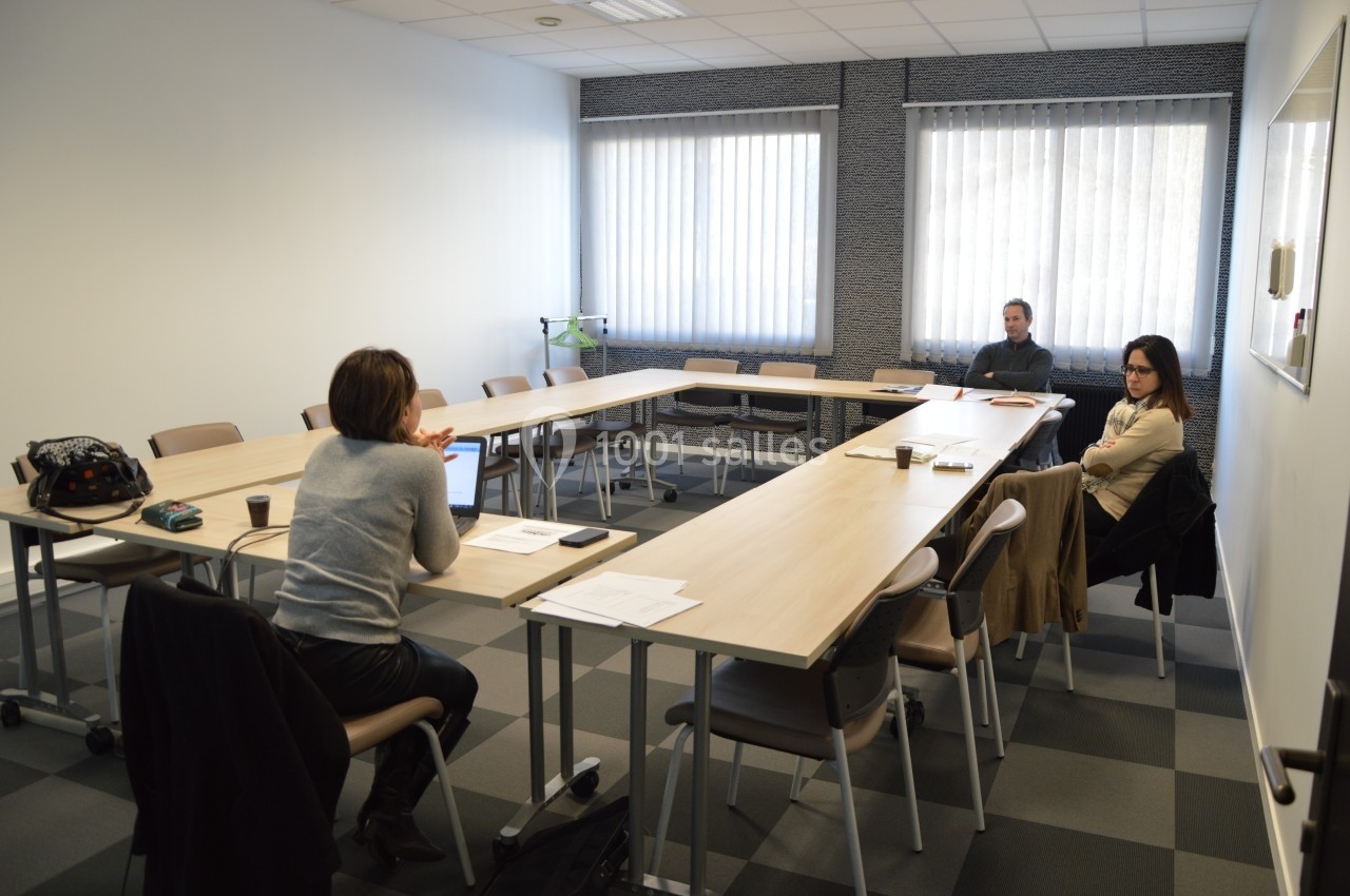 Une réunion dans une salle lumineuse avec trois personnes assises autour de tables en U.