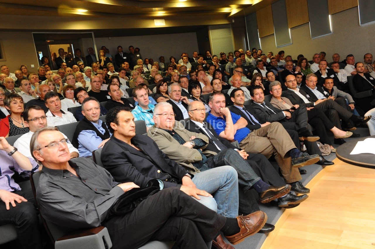 Un public nombreux assis dans une salle de conférence, attentif à une présentation hors champ.
