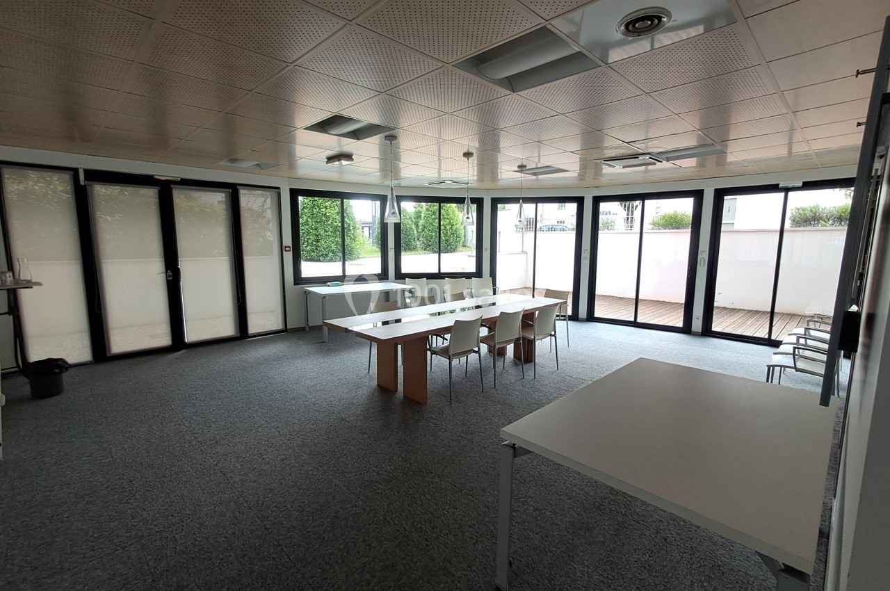 Salle de réunion lumineuse avec une grande table, des chaises et des baies vitrées donnant sur une terrasse.