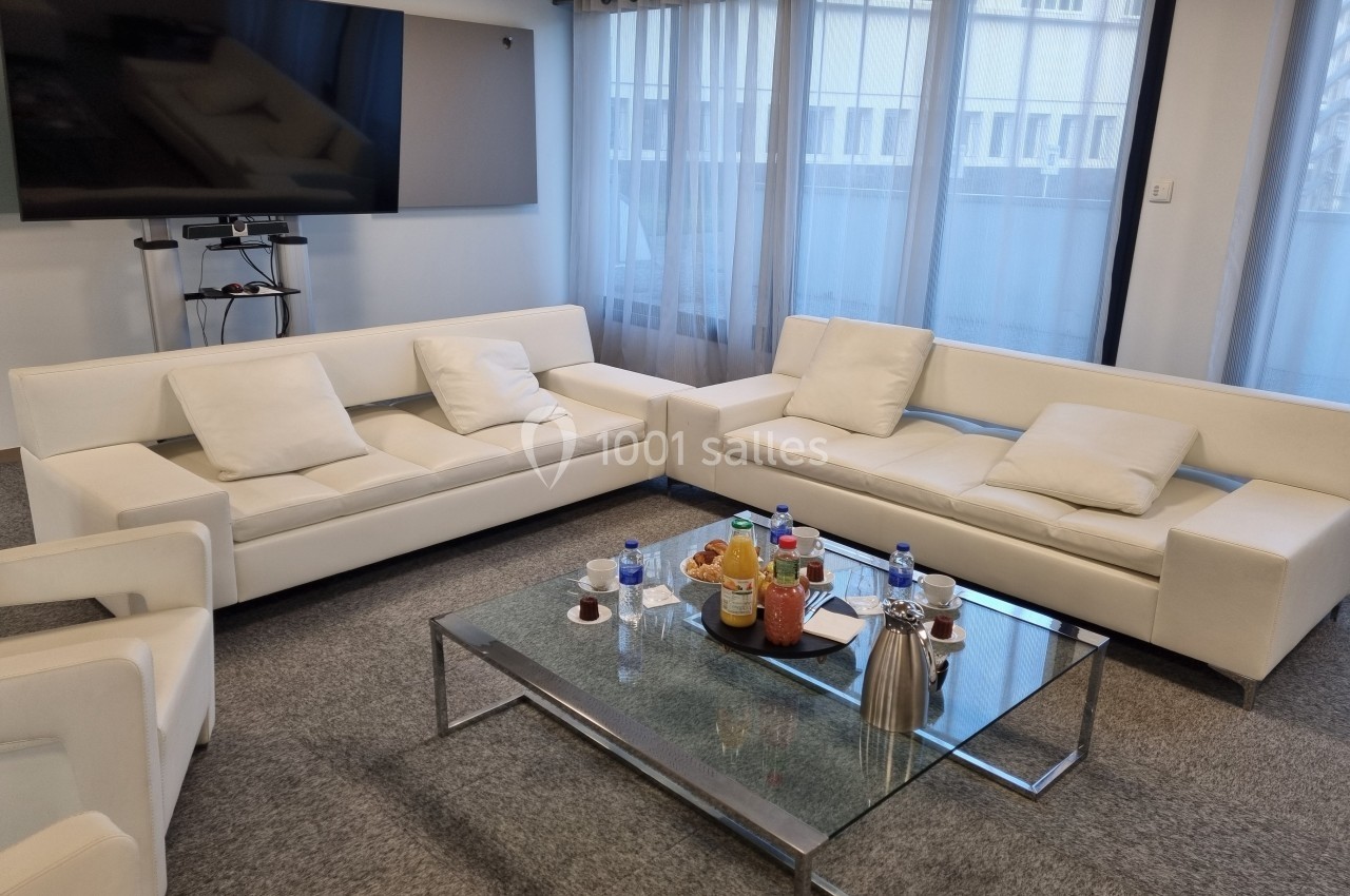 Deux canapés blancs autour d'une table basse en verre avec boissons et collations, dans une salle lumineuse.