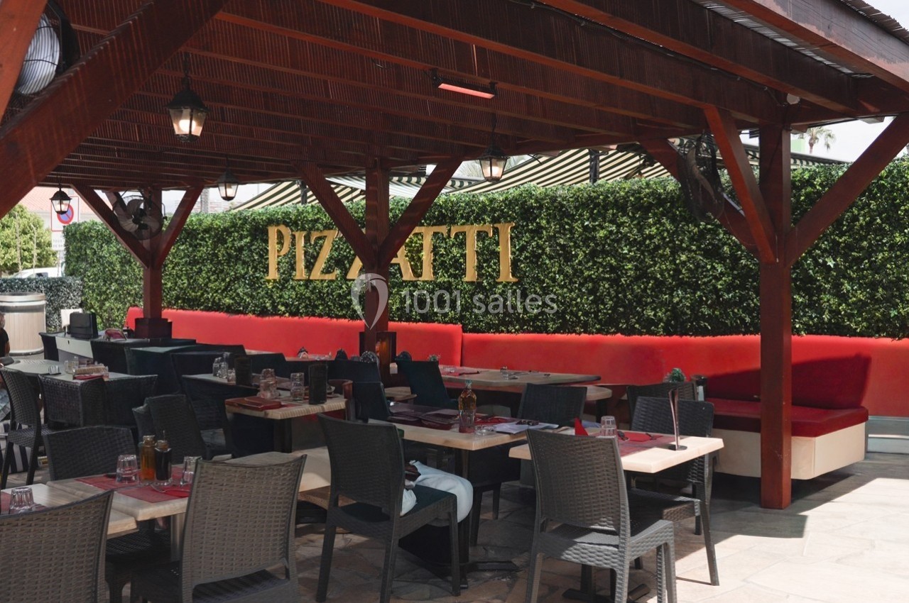 Location salle Villeneuve-Loubet (Alpes-Maritimes) - Pizzatti Villeneuve Loubet #3 Terrasse d'un restaurant avec tables dressées, banquettes rouges et mur végétal portant l'inscription ’Pizzatti’.