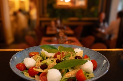 Assiette contenant un tartare de viande, des tranches de jambon cru et une salade verte avec une tomate cerise.
