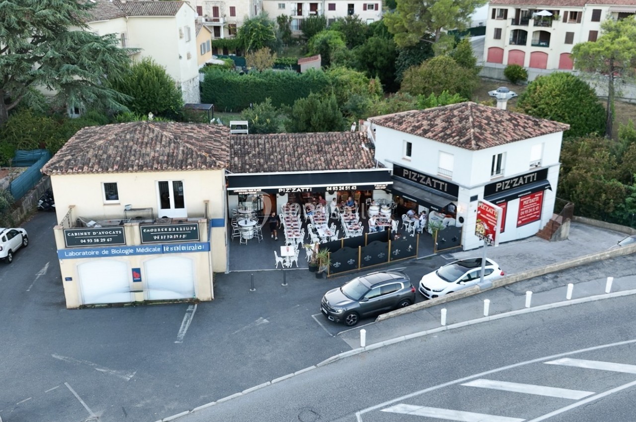 Vue aérienne d'un restaurant avec terrasse extérieure, entouré de bâtiments et de voitures stationnées.