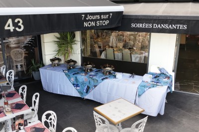 Table dressée avec nappes blanches, serviettes bleues, verres, couverts et décorations florales colorées.