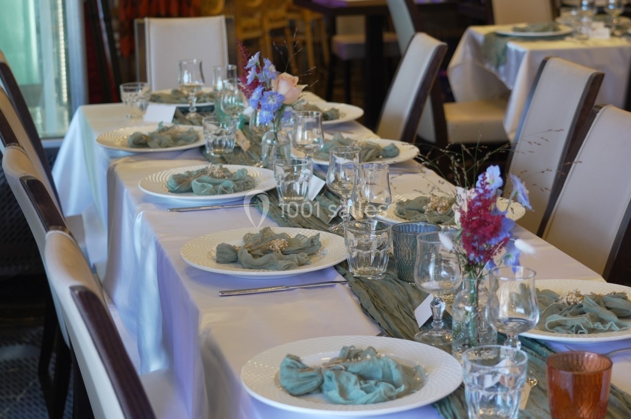 Table dressée avec nappes blanches, serviettes vertes, vaisselle élégante et décoration florale au centre.