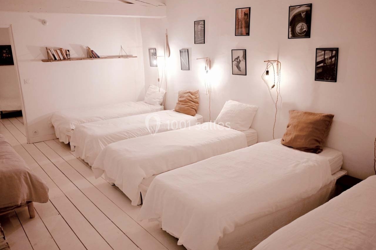 Chambre lumineuse avec cinq lits simples alignés, décorée de cadres, étagères et éclairages muraux.