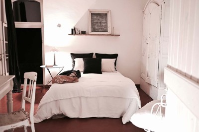 Quatre lits simples alignés dans une chambre lumineuse avec murs blancs, décor minimaliste et poutres apparentes.