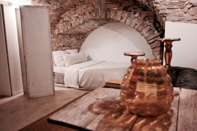 Quatre lits simples alignés dans une chambre lumineuse avec murs blancs, décor minimaliste et poutres apparentes.