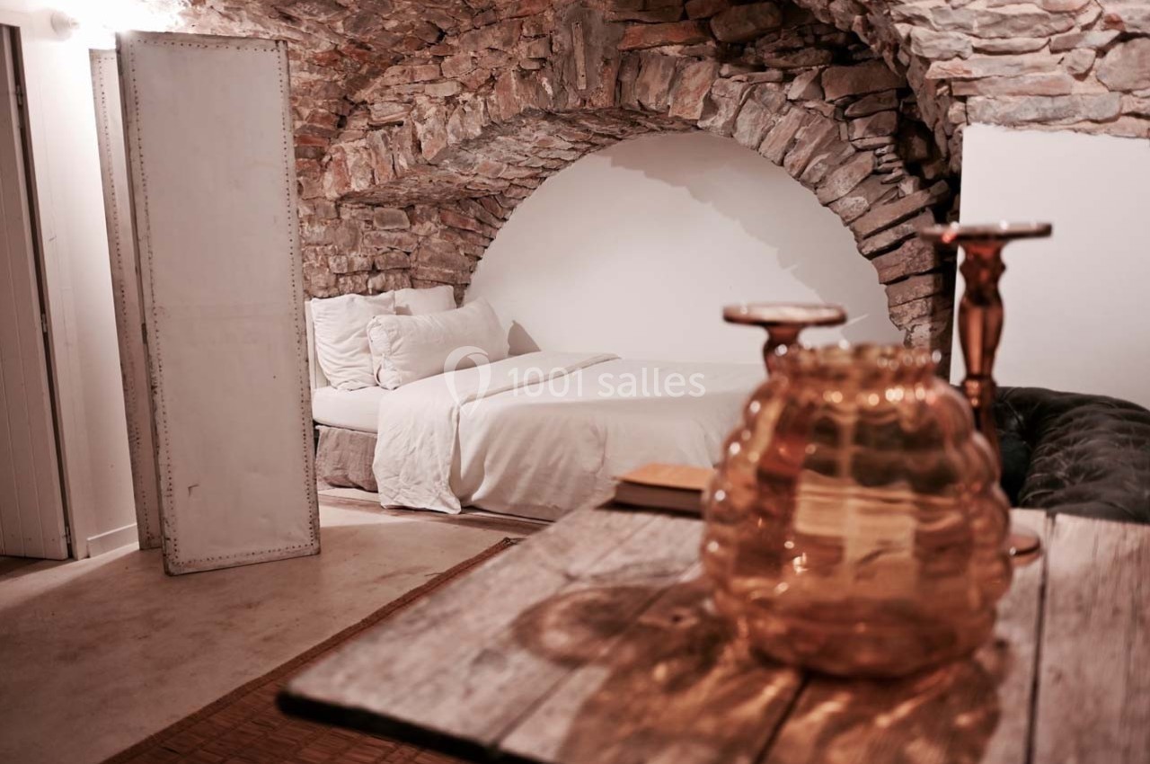 Chambre avec lit double sous une voûte en pierre, décorée avec des objets en verre sur une table en bois.
