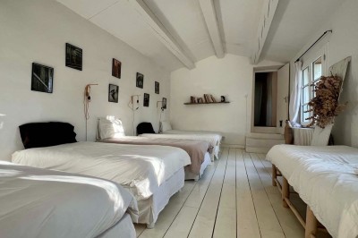 Quatre lits simples alignés dans une chambre lumineuse avec murs blancs, décor minimaliste et poutres apparentes.