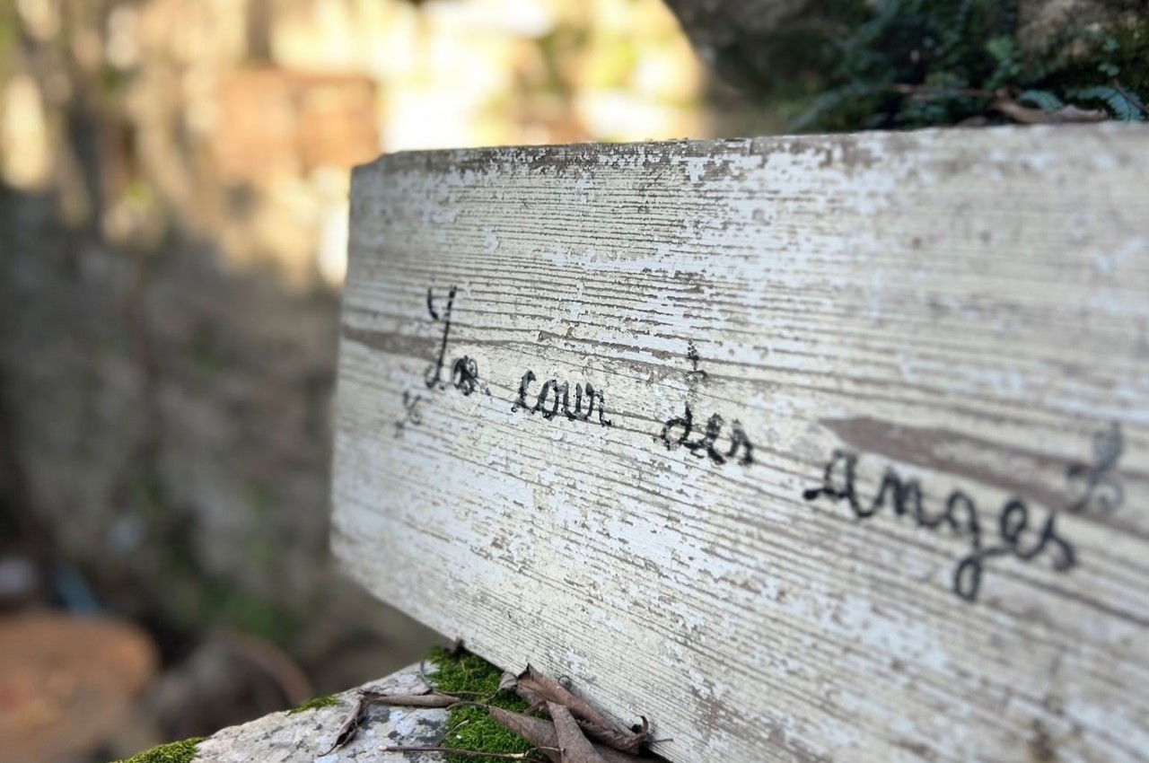 Pancarte en bois vieilli avec l'inscription manuscrite ’La cour des anges’, posée dans un environnement naturel.