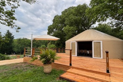Tente de style yourte avec terrasse en bois, entourée d'arbres dans un cadre naturel.