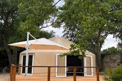 Tente de style yourte avec terrasse en bois, entourée d'arbres dans un cadre naturel.