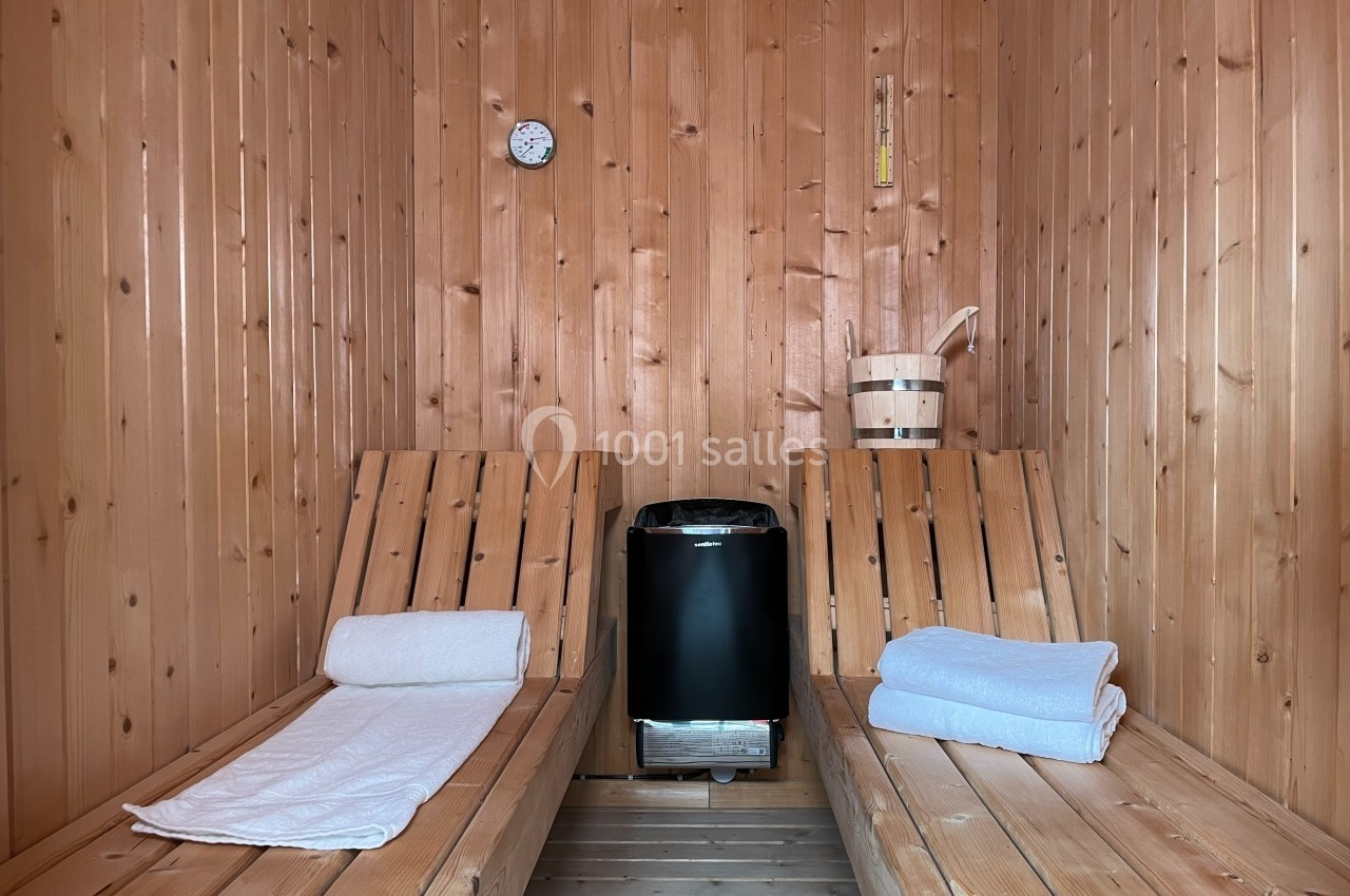 Intérieur d'un sauna en bois avec deux bancs, des serviettes pliées et un poêle au centre.