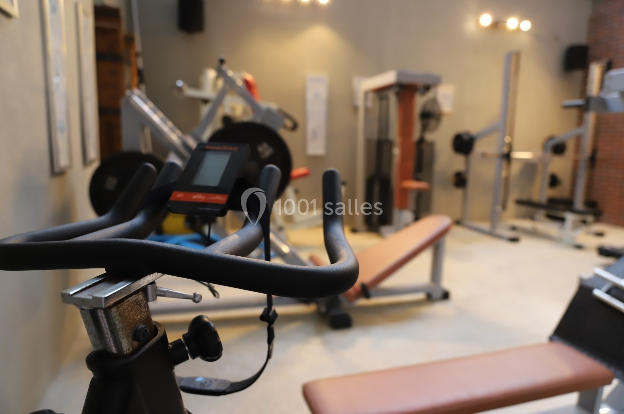 Salle de sport avec équipements de musculation et vélo d'exercice au premier plan.