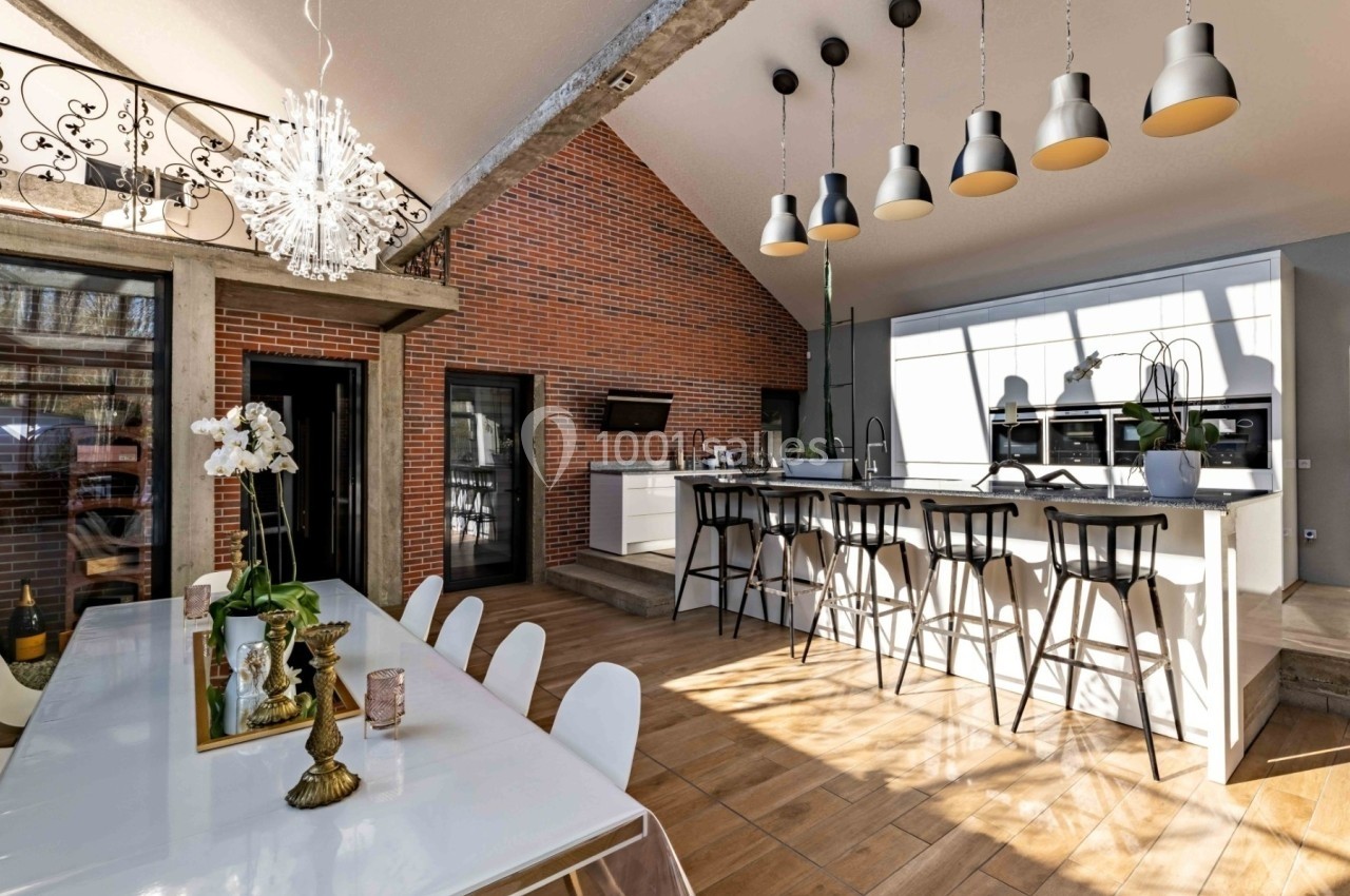 Cuisine ouverte moderne avec îlot central, table à manger, mur en briques et luminaires suspendus.