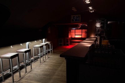 Bar en bois sombre avec comptoir équipé de crochets, étagères à verres et tableau noir affichant le menu.