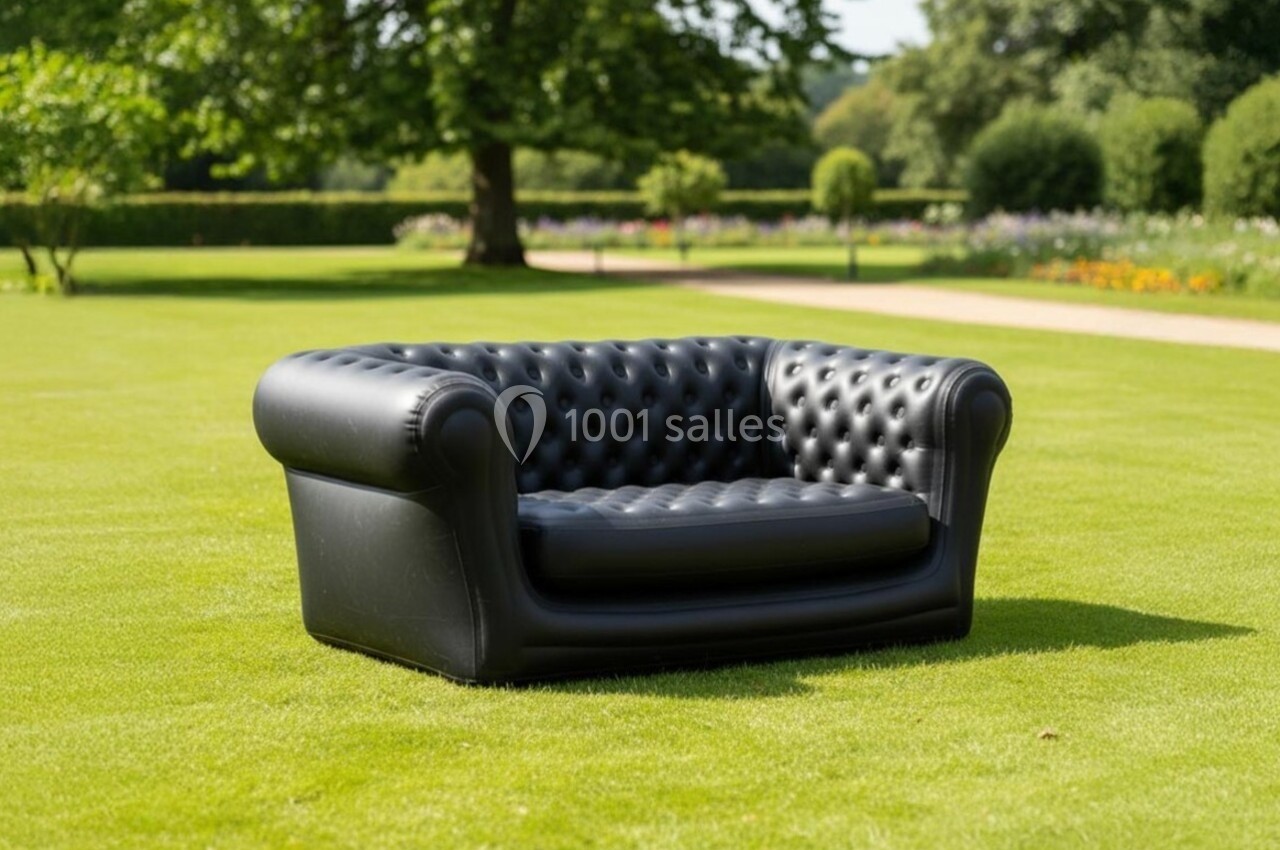 Canapé Chesterfield noir en cuir capitonné placé sur une pelouse verte dans un jardin arboré.