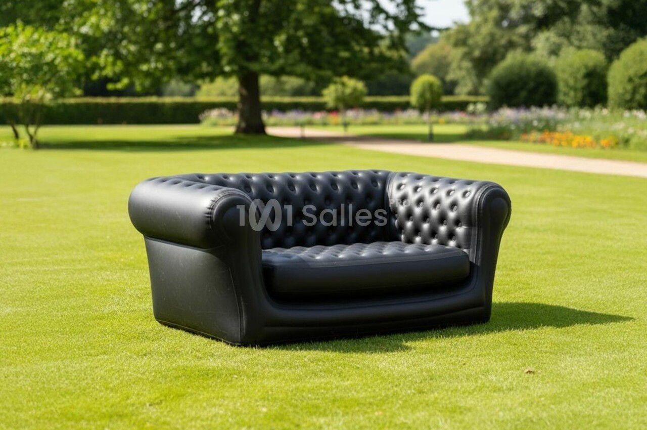 Canapé Chesterfield noir en cuir capitonné placé sur une pelouse verte dans un jardin arboré.