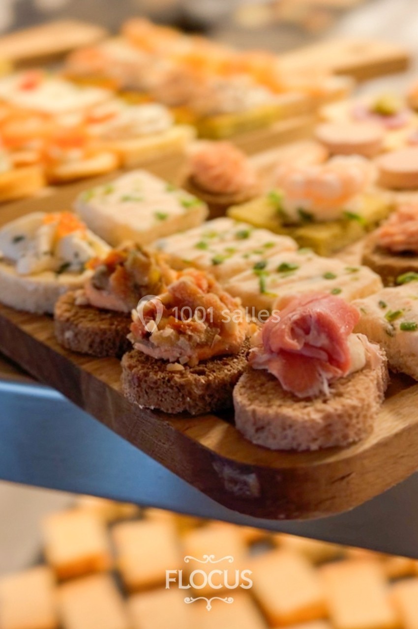 Plateau de canapés variés avec garnitures de crevettes, jambon et fromage, présenté sur une planche en bois.