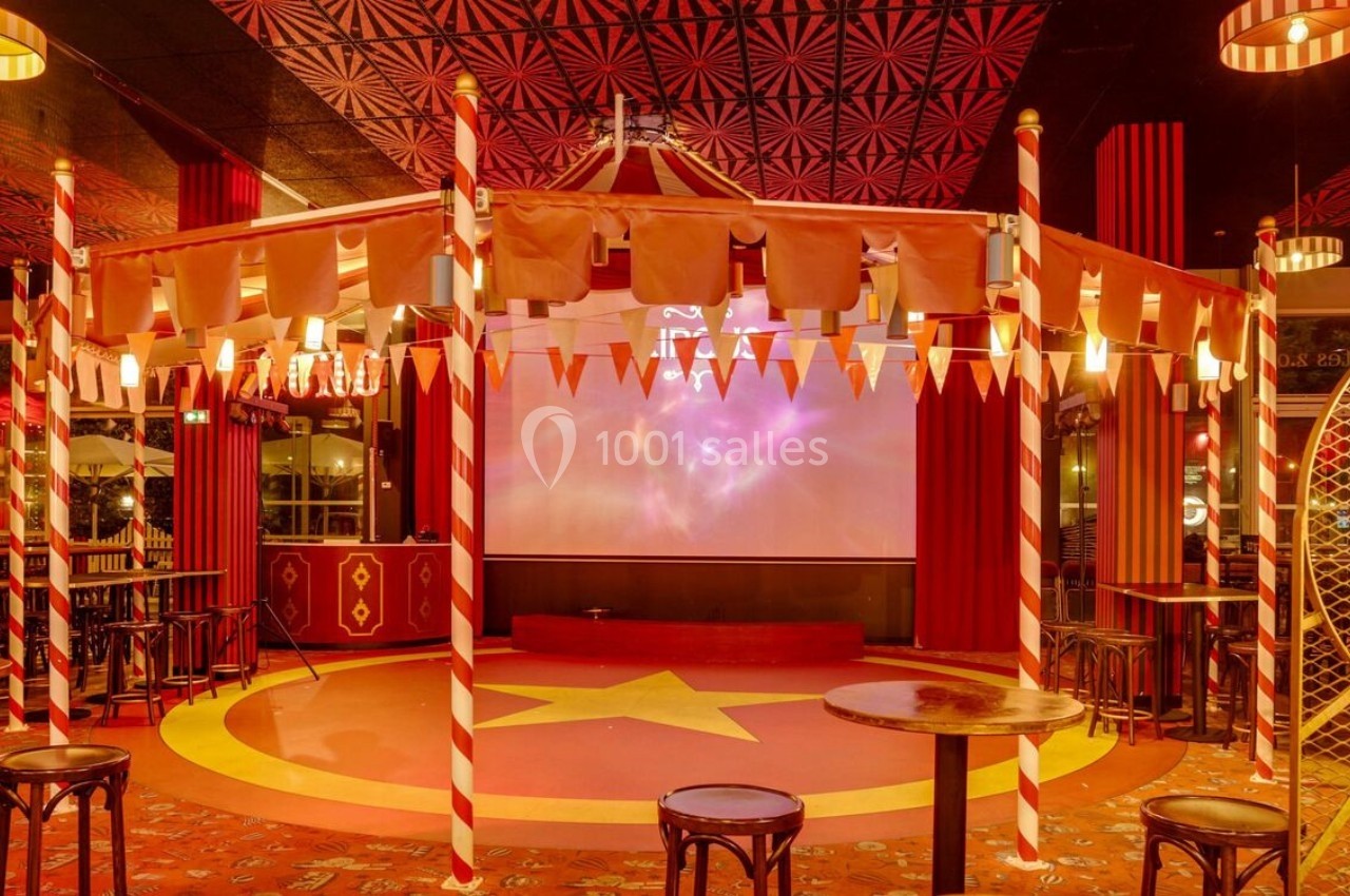 Intérieur d'une salle décorée sur le thème du cirque avec chapiteau, estrade étoilée et tabourets autour de tables.