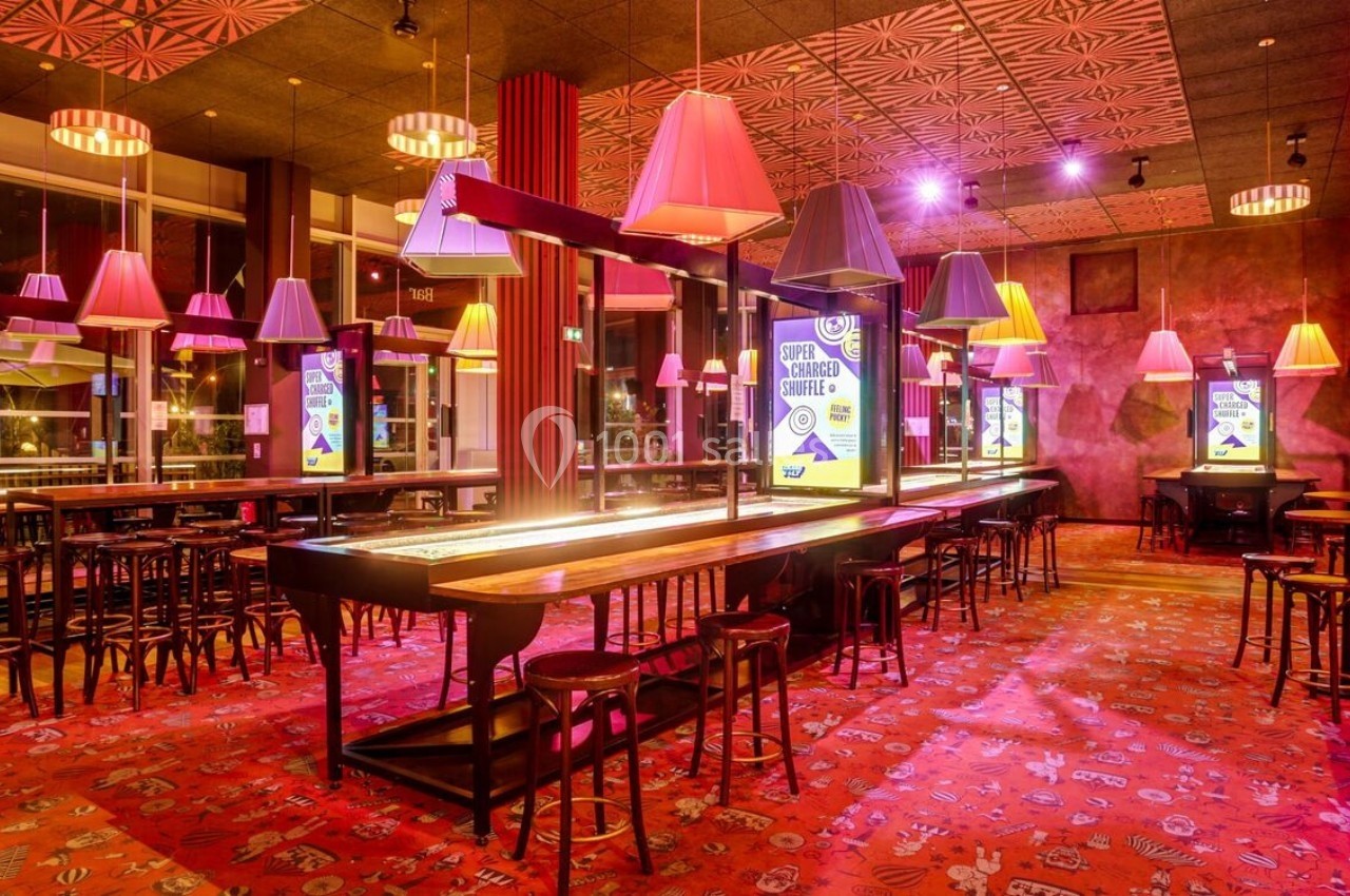 Salle de bar moderne avec éclairage coloré, tables hautes, tabourets et décorations lumineuses suspendues.