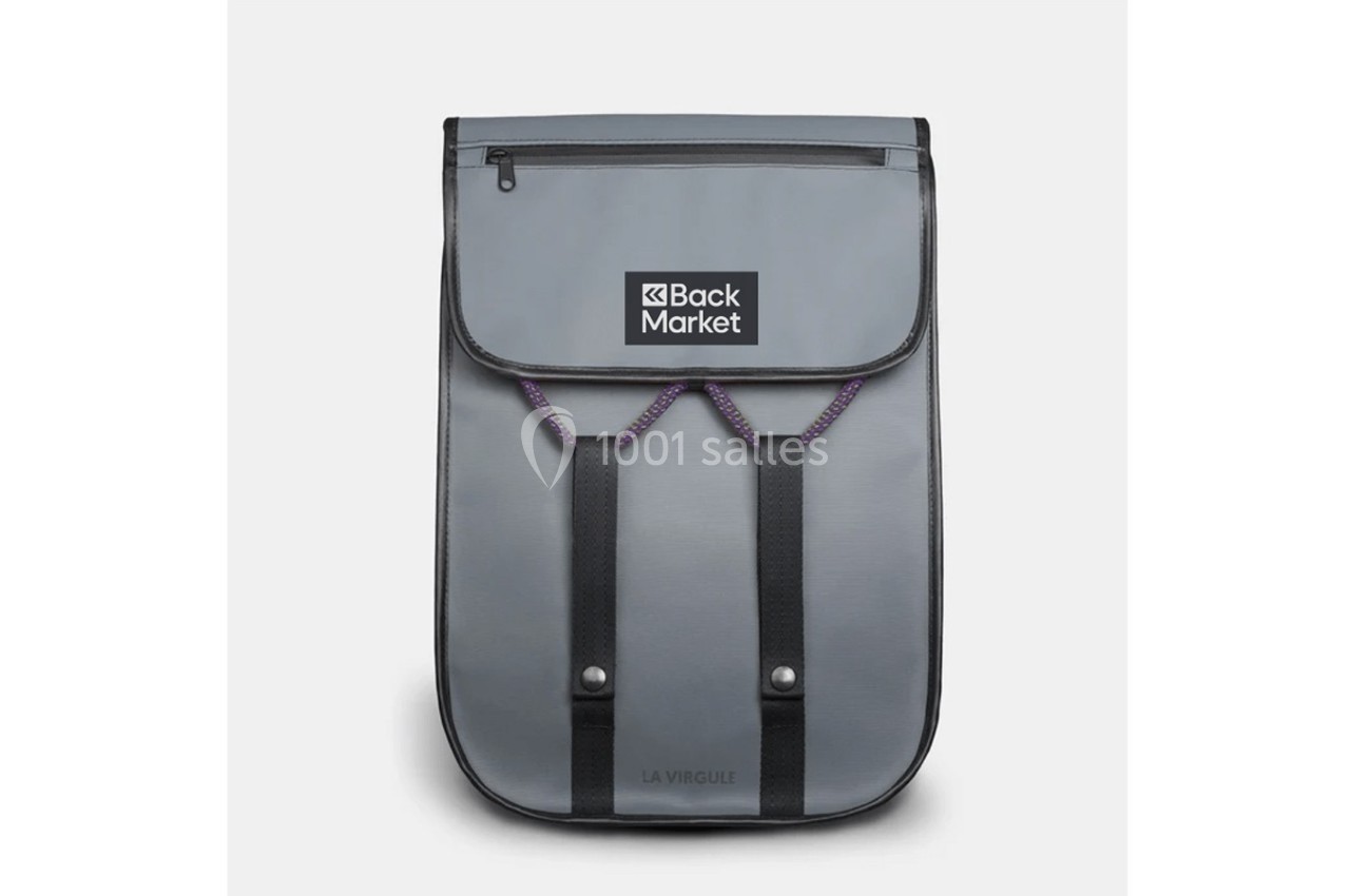 Sac à dos gris avec rabat, logo ’Back Market’ visible, deux sangles noires et une poche zippée sur le dessus.