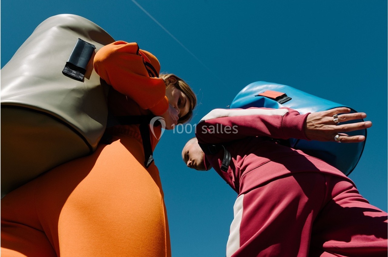 Deux personnes en tenue colorée portant de grands sacs à dos, vues en contre-plongée sous un ciel bleu.